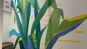 A wall with a large abstract painting of green and blue leaves with yellow lines.