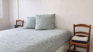 A bedroom with a bed, two pillows, a chair, and an air conditioning unit.