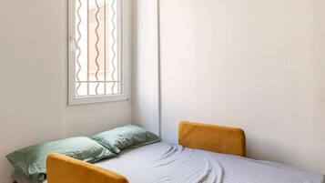 Une petite chambre avec un lit simple, une fenêtre et un appareil de climatisation.