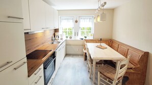 A kitchen with a wooden countertop, white cabinets, a built-in oven, a dining table with chairs, and a window with curtains. - FeWo Merle Altastenberg – Nature & Active Holidays (Winterberg)