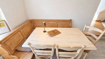 Una zona pranzo angolare con un tavolo in legno, quattro sedie e una panca, illuminata da una lampada.