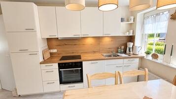 Eine moderne Küche mit weißen Schränken, einer Holz Arbeitsplatte, einem eingebauten Backofen, einem Spülbecken und Pendelleuchten.