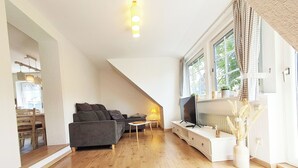 A modern living room with a sofa, TV, and a dining area visible through an open door. - FeWo Merle Altastenberg – Nature & Active Holidays (Winterberg)