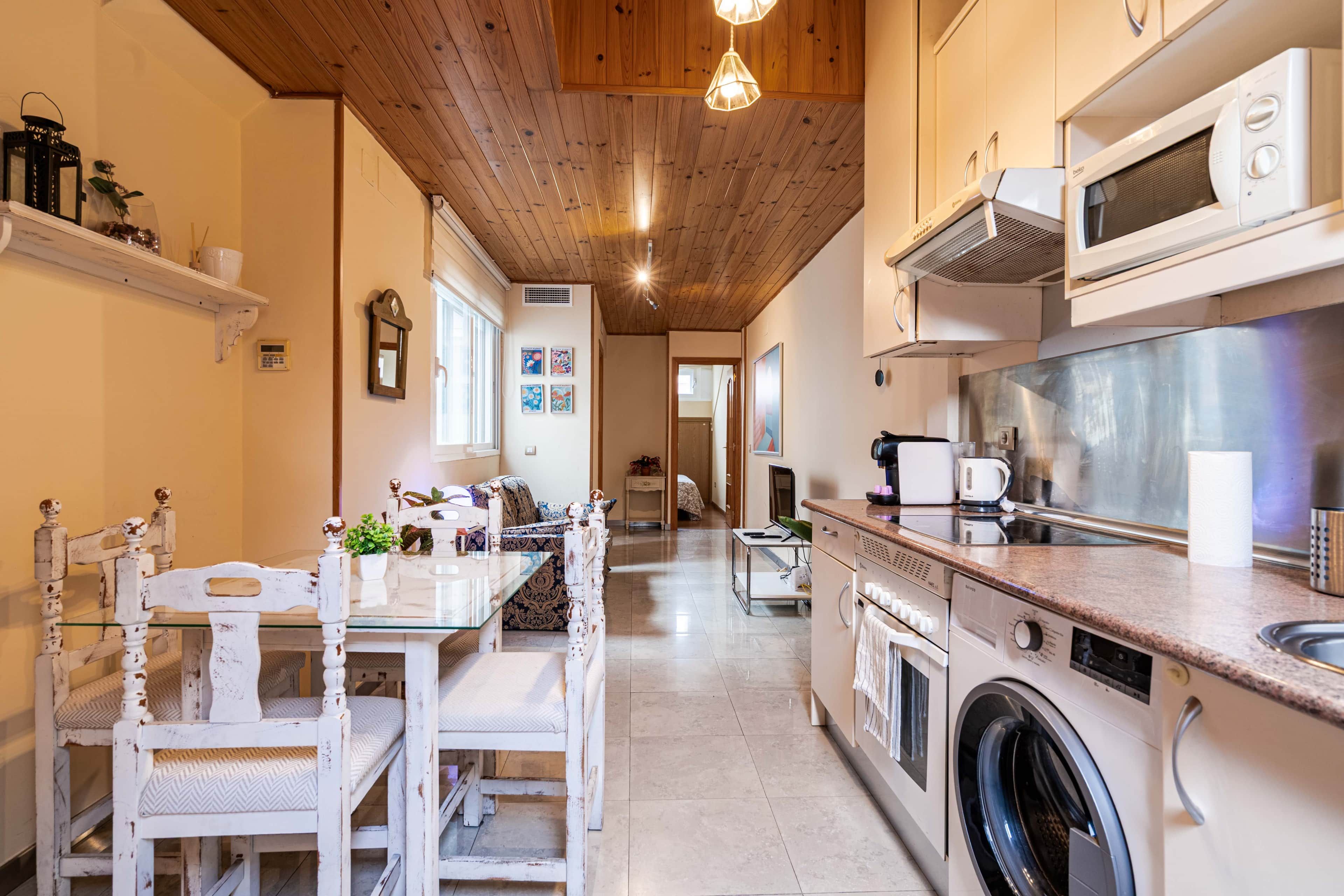 A kitchen with a washing machine, microwave, and wooden ceiling.