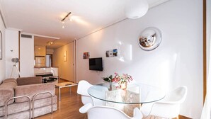 A modern living room with a glass dining table, white chairs, a sofa, and a kitchen in the background. - Apartment. Balcony, bright, centrally located (Madrid)