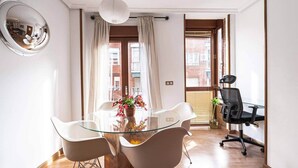 A modern room with a glass table, white chairs, a black office chair, a round mirror, and a view of a building through a window. - Apartment. Balcony, bright, centrally located (Madrid)