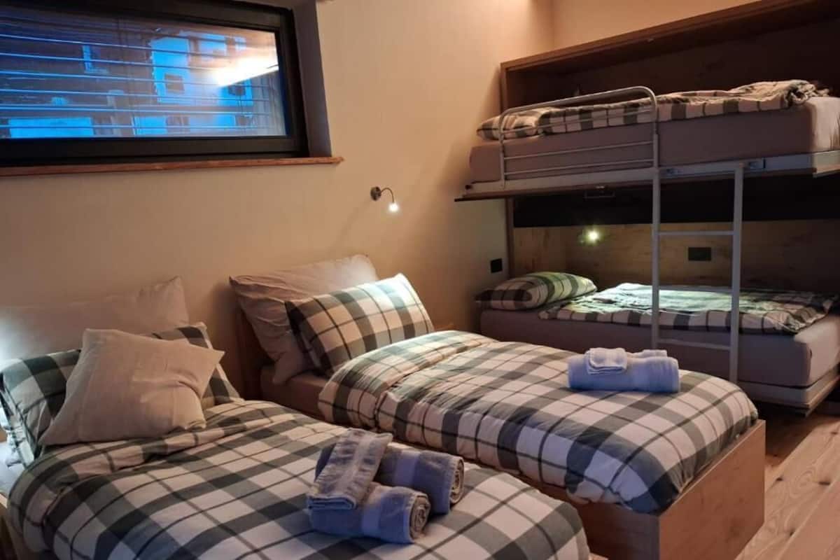 A room with two single beds, a bunk bed, and a television mounted on the wall.