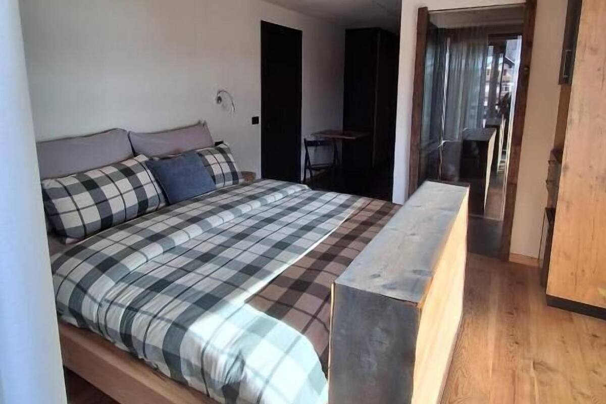 A bedroom with a wooden bed, a bench, and a doorway leading to another room.