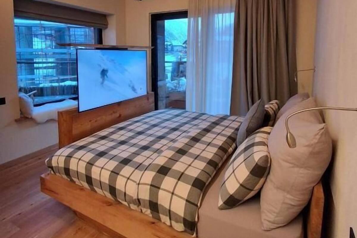 A bedroom with a wooden bed, a television, a window, and curtains.
