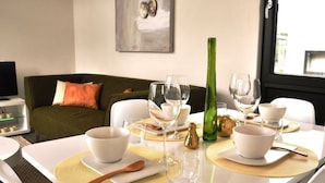 Ein Esstisch ist gedeckt mit weißen Schüsseln, Gläsern und einer grünen Flasche, im Hintergrund ein grünes Sofa und ein Gemälde.
