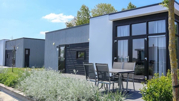 Ein modernes Gebäude mit Flachdach, großen Fenstern und einer Terrasse mit Sitzgelegenheiten.
