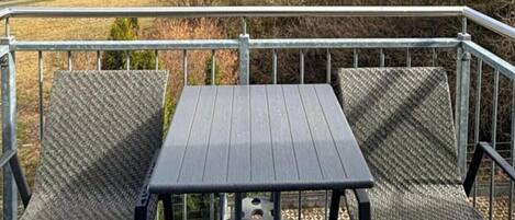 A deck with a table and chairs, overlooking a hilly landscape with trees and buildings in the distance.