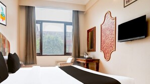 Habitación de hotel con una cama grande, un televisor de pantalla plana, un escritorio con espejo y una ventana con cortinas.