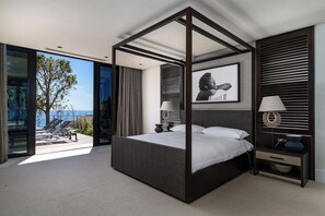 A modern bedroom with a four-poster bed, a large window, and a view of the outdoors. - Halcyon Villa (Cape Town)