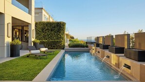 Zona de piscina exterior moderna amb vista despejada al mar, gespa ben cuidada i mobiliari relaxant.