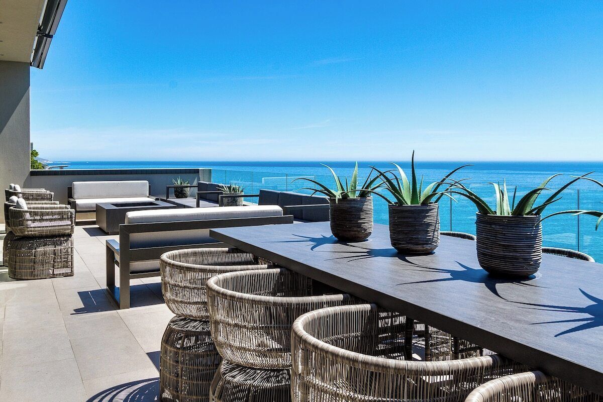 Un espace extérieur aménagé avec des meubles en osier et des plantes en pot, offrant une vue sur une mer d’un bleu limpide.
