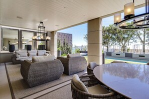 An outdoor patio with wicker furniture, a dining table, and a pool in the background. - Halcyon Villa (Cape Town)
