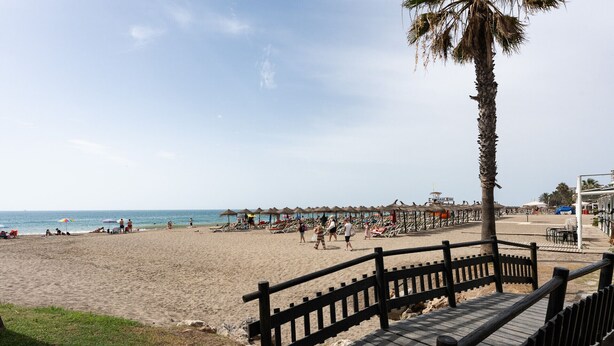 Ein Strand mit einer Holzpromenade, Palmen und Strandstühlen.
