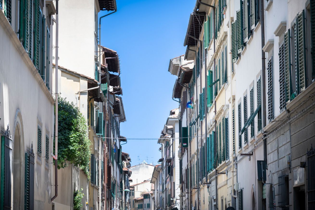 Une rue étroite bordée d’immeubles aux volets verts et aux balcons.