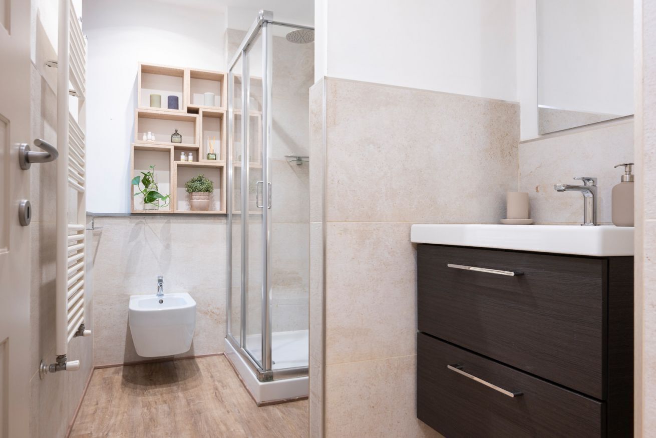 A modern bathroom with a glass shower enclosure, a bidet, and a dark wood vanity.