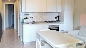 A modern kitchen with white cabinets, a gas stove, and a dining area with a white table and chairs. - Ligurian Oasis (Pietra Ligure)
