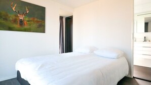 Quarto de hotel moderno com uma cama grande, um quadro de um veado, um banheiro com espelho e piso de madeira escura.