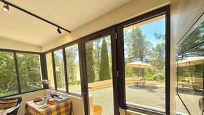 Una habitación iluminada por el sol, con ventanas amplias, una mesa con mantel a cuadros y una zona de estar exterior con sombrilla.