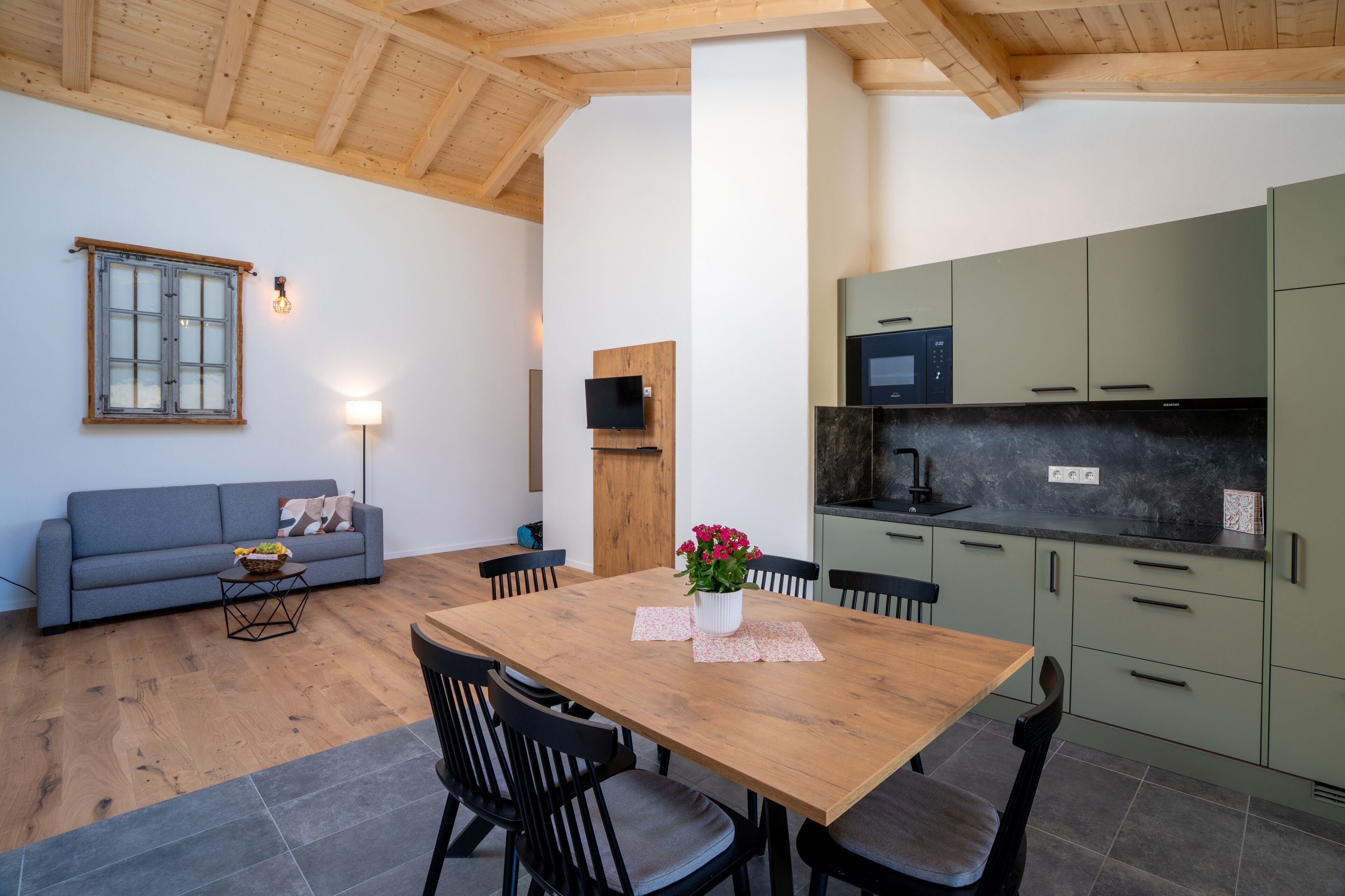 Un espacio habitable compacto con mesa de comedor, sillas, sofá, televisor y kitchenette.