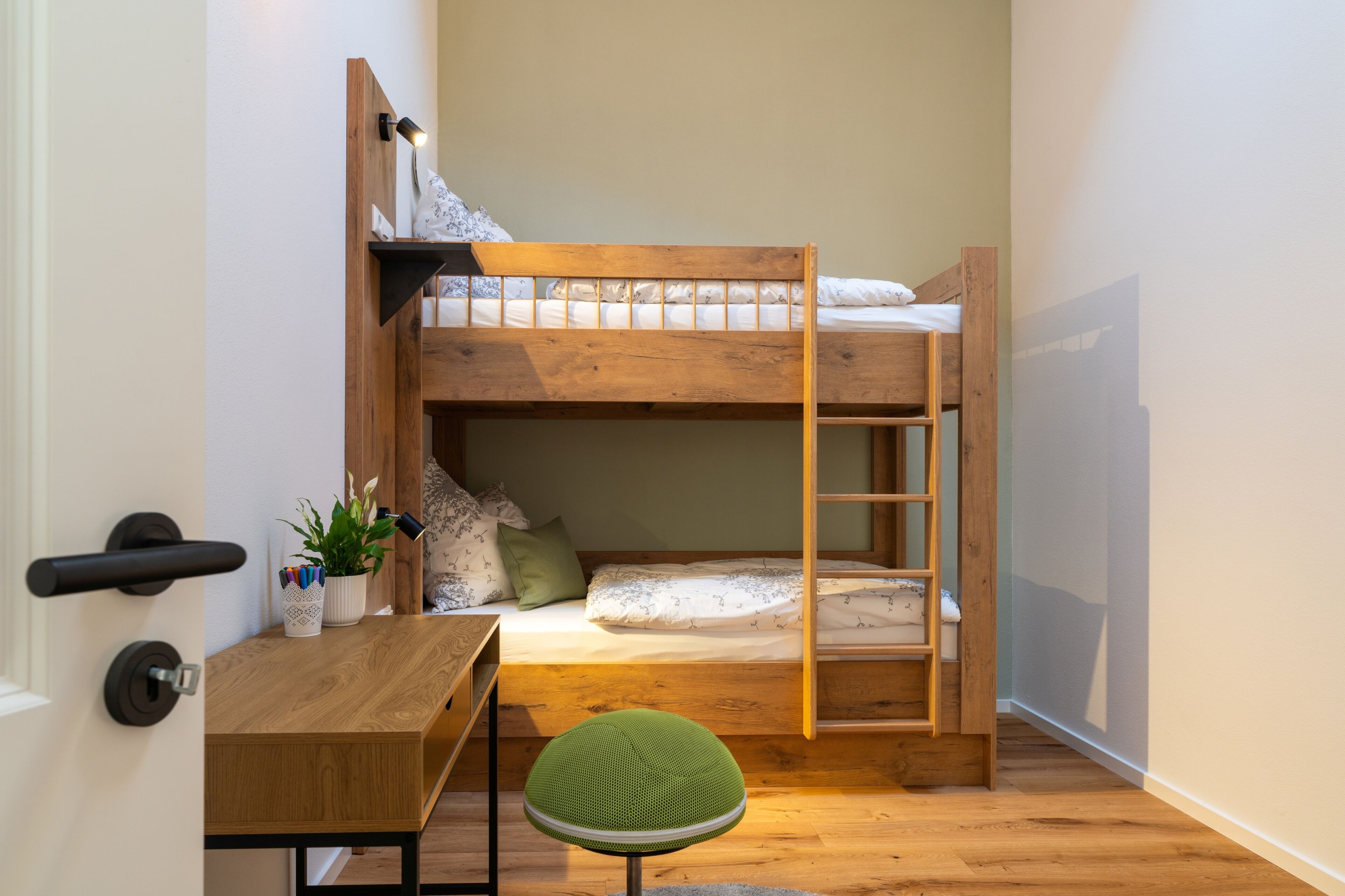 A bunk bed with a desk and chair, a small plant, and a ladder.