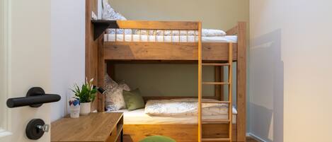 A bunk bed with a desk and chair, a small plant, and a ladder.