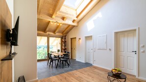 Una habitación amplia con techo de madera, una zona de comedor con mesa y sillas, y vistas a través de un ventanal grande.