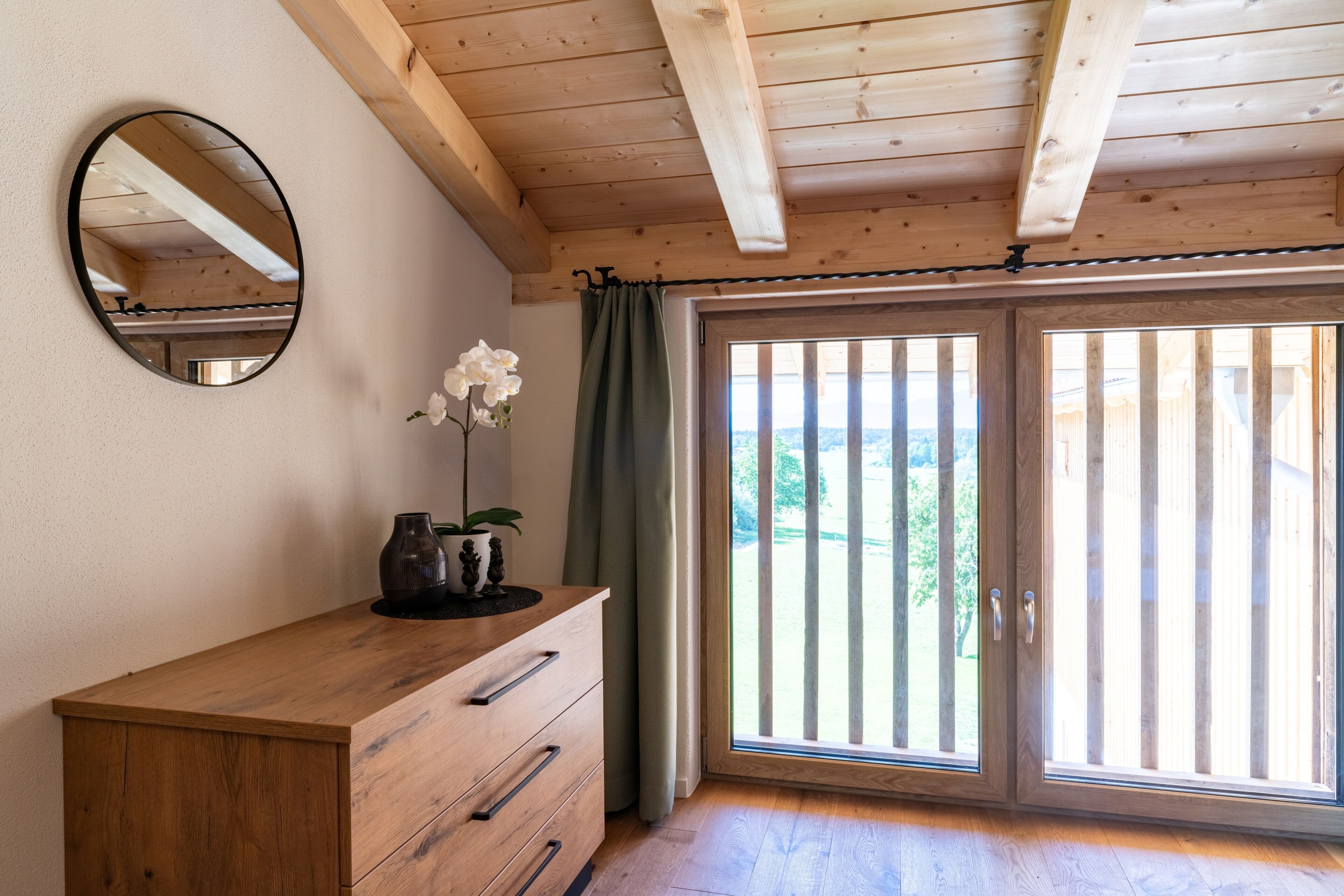 Ein Zimmer mit einem Holzkasten, einem Spiegel, einer Topfpflanze und einer Glastür, die zu einem Außenbereich führt.
