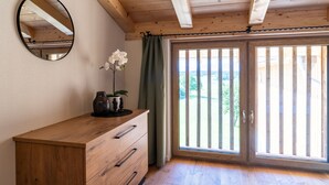 Una habitación con un aparador de madera, un espejo, una planta en maceta y un ventanal corredero que da a un espacio exterior.