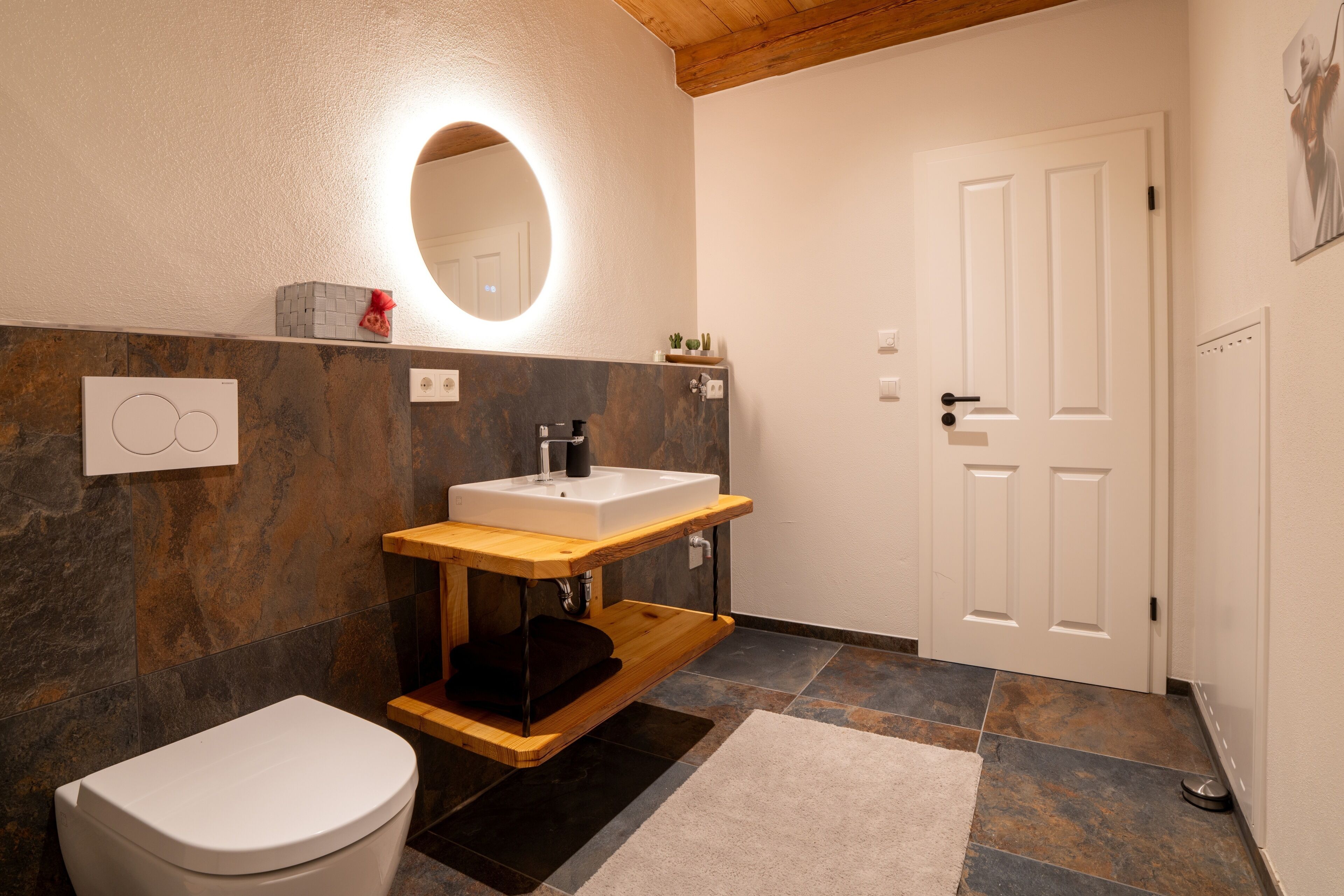 A bathroom with a white toilet, a wooden vanity with a sink, a mirror, and a door.