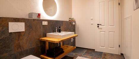 A bathroom with a white toilet, a wooden vanity with a sink, a mirror, and a door.