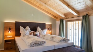 Ein Schlafzimmer mit Holzbalkendecke, einem Bett mit Kopfteil, Nachttischlampen, einer Bank und einem Fenster mit Vorhängen.