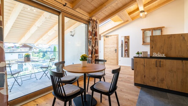 Ein modernes Interieur mit Holzboden, einem runden Esstisch mit Stühlen, einer Küchenzeile und einer Schiebeglastür zum Außenbereich.
