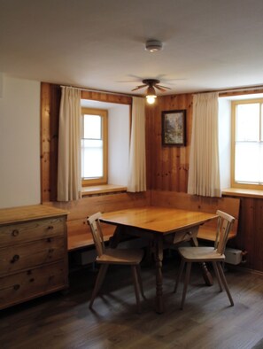Une salle à manger avec une table et des chaises en bois, un ventilateur de plafond et des fenêtres avec des rideaux.