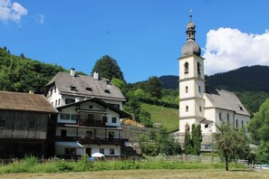 A traditional building with a prominent tower, surrounded by lush greenery and hills. - Steinberg Vacation Rental (Ramsau bei Berchtesgaden)