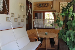 Un banc en bois avec une chaîne suspendue, une petite table ronde en bois et une fenêtre ornée de rideaux en dentelle.