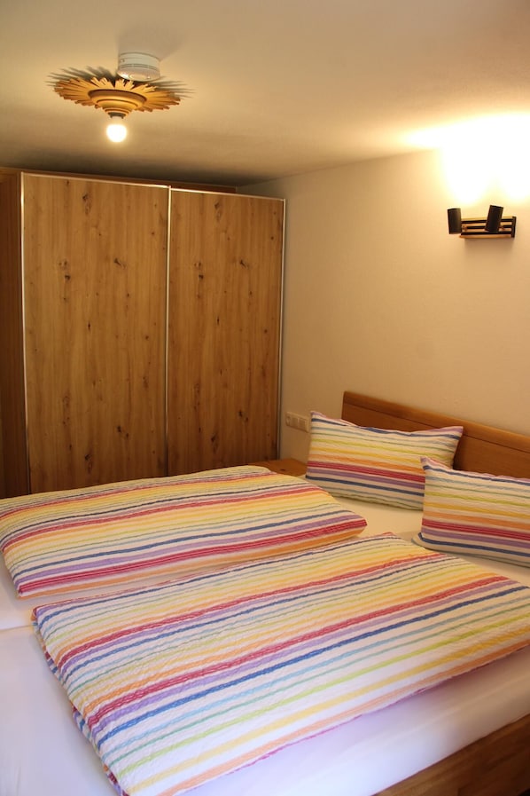 Une chambre à coucher avec un lit, une literie à rayures, une armoire en bois et un luminaire fixé au plafond.