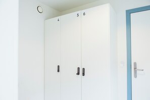 Una habitación blanca con una puerta azul, taquillas numeradas y un interruptor de luz en la pared.