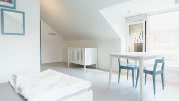 Een kamer met een wit ledikant, een witte tafel met blauwe stoelen en een bed met witte lakens.