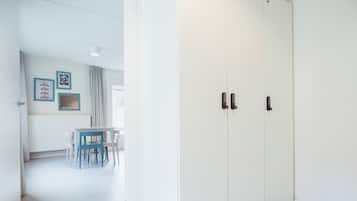 Una habitación con un armario blanco, una mesa con sillas y un ventanal con cortinas.