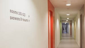 Corredor com sinalização indicando quartos 101 a 113 e chuveiros e sanitários.