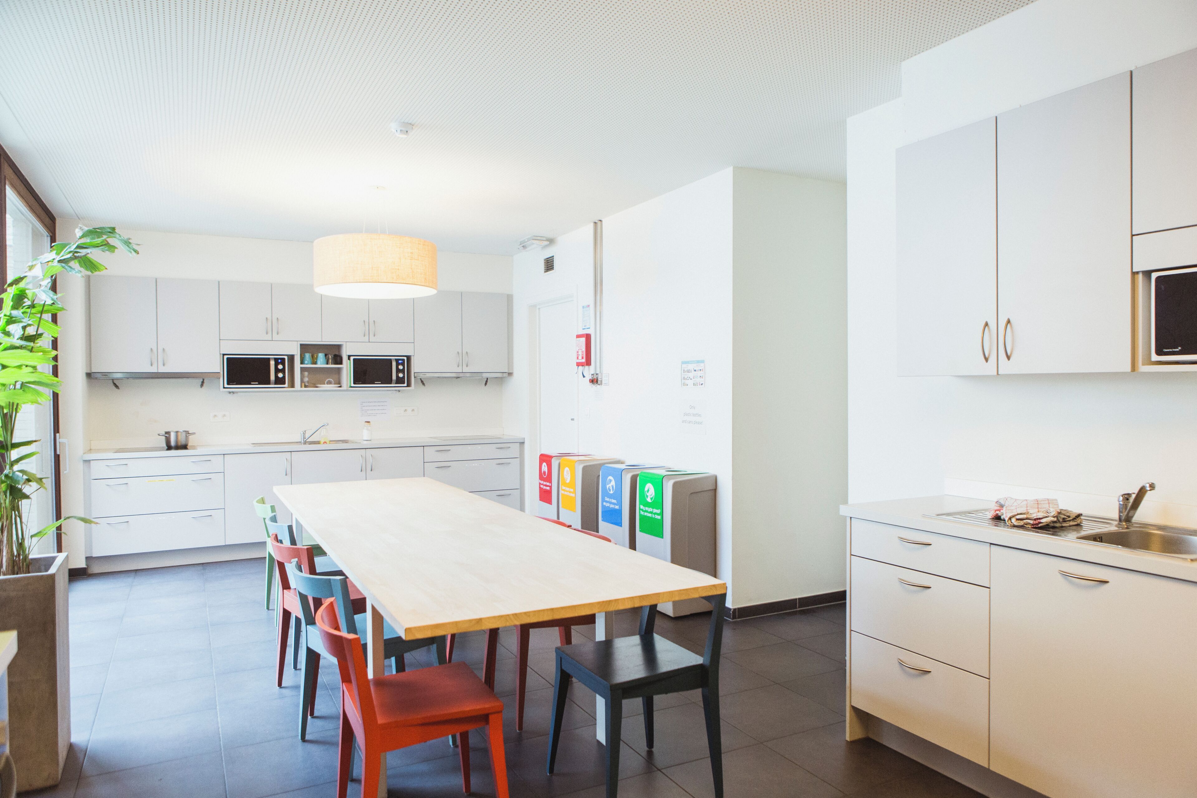 Una cocina moderna con armarios blancos, una mesa de madera y sillas coloridas.