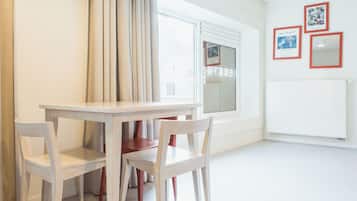 Une pièce avec une table et des chaises blanches, une fenêtre avec des rideaux et un mur orné de tableaux encadrés.