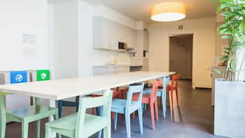 Een moderne keuken met witte kasten, een magnetron en een spoelbak. Er is een eethoek met een lange tafel en kleurrijke stoelen.