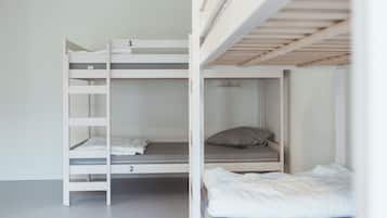 Een stapelbed met twee niveaus, een klein plankje en een enkel bed met een kussen.