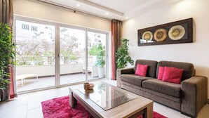 Un salon moderne avec un canapé, une table basse en verre et une grande porte-fenêtre coulissante donnant sur un balcon.